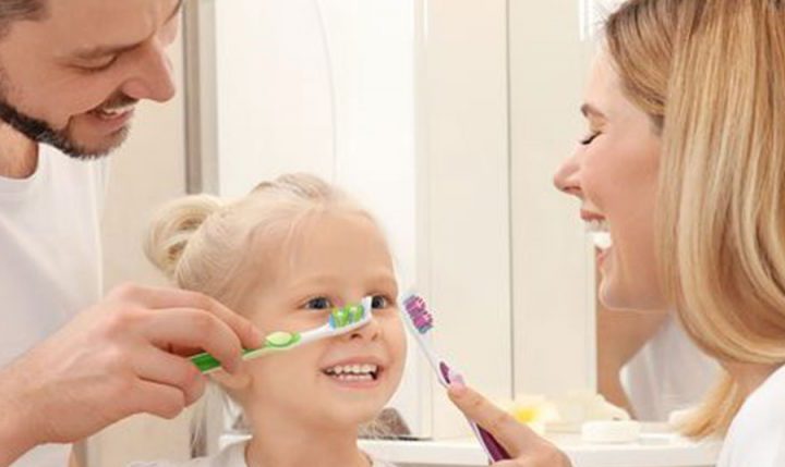 mum and dad helping small child brush her teeth in the bathroom